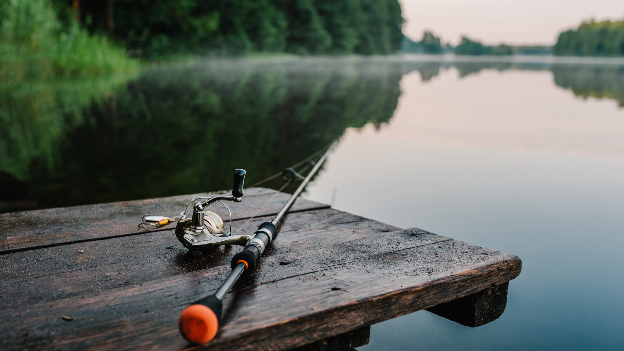 Fishing rod, spinning reel on the background pier river bank. Sunrise. Nebel vor dem Hintergrund des Sees. Misty morning. wilde Natur. Das Konzept des ländlichen Gehöfts. Artikel über den Angeltag.      